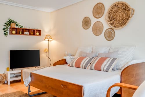 Quarto luminoso na AlgarStays Pine Sun 29 em Silves com cama de madeira, almofadas listradas, cestos tecidos na parede, TV e vista para o jardim