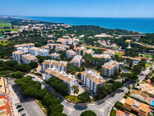 Vista aérea dos apartamentos AlgarStays em Silves, Portugal com oceano turquesa, jardins verdes e edifícios brancos
