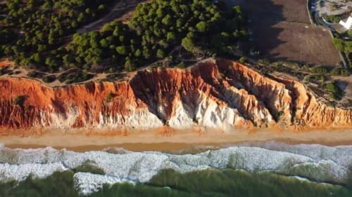 Falésias costeiras dramaticamente listradas em vermelho e branco em Silves, Portugal com praia e ondas oceânicas abaixo