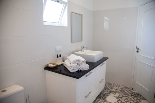 Modern bathroom at Casa Branco, MarVillas Rentals in Lagoa with white vanity, black countertop, and rolled towels