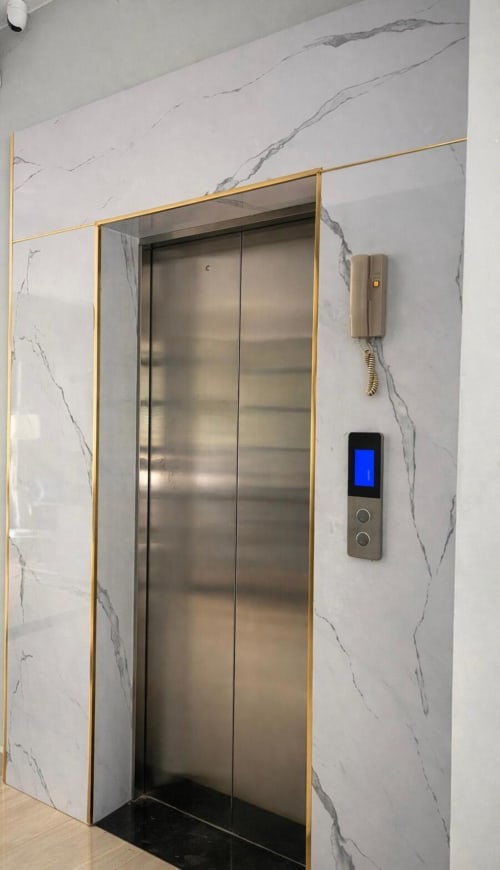 Entrée d'ascenseur moderne aux encadrements dorés et murs en marbre à l'hôtel Cybade, Phu Quoc
