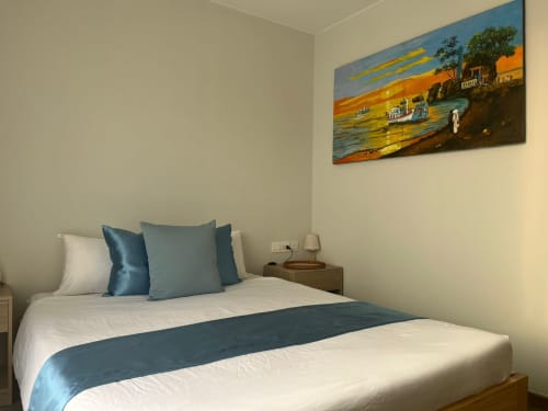 Lit queen-size avec vue sur mer à l'hôtel Cybade, Phu Quoc. Chambre moderne avec accents bleus, œuvre d'art, table de nuit et décoration côtière.
