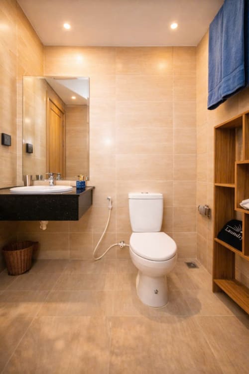 Salle de bain moderne au Cybade Hôtel Phu Quoc avec carrelage beige, toilettes blanches, lavabo rond, miroir et étagères en bois