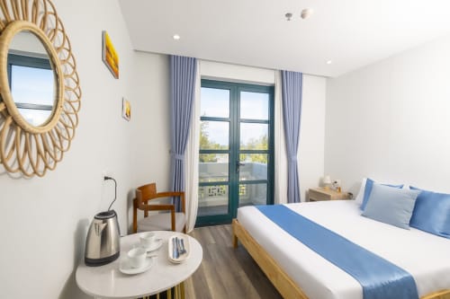Chambre Queen Cybade Hôtel Phu Quoc avec accents bleus, balcon, miroir en rotin et équipements modernes