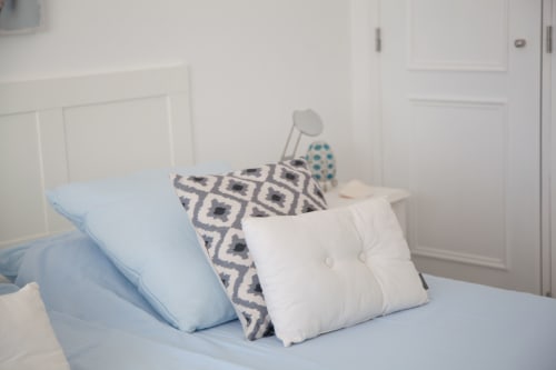 Quarto com almofadas azul-claro e almofadões estampados em cama branca na MarVillas Rentals em Lagoa