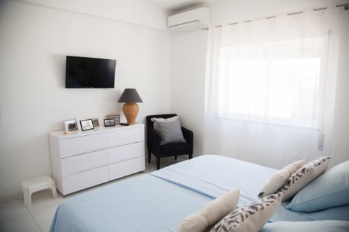 Quarto moderno em MarVillas Rentals em Lagoa com cama, cômoda branca, TV, cadeira preta e muita luz natural