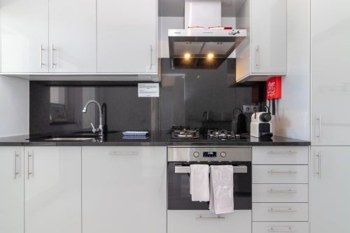 Cozinha moderna branca com bancada preta, fogão a gás, coifa e pia em MarVillas Rentals em Lagoa