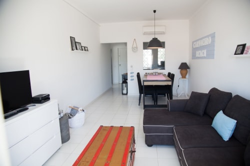 Sala de estar moderna na propriedade de aluguel MarVillas, Lagoa Portugal, com sofá preto, TV, mesa de jantar e cozinha integrada