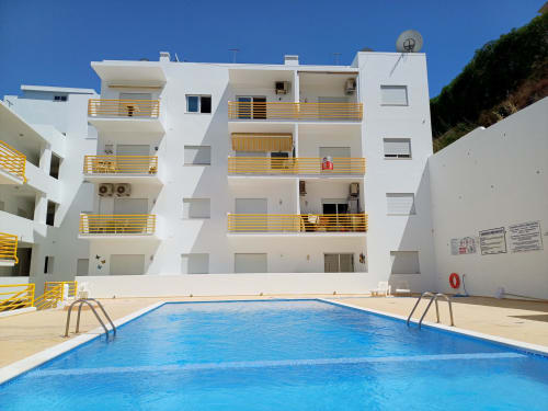 Complexo de apartamentos MarVillas em Lagoa com piscina azul, varandas brancas e corrimões amarelos