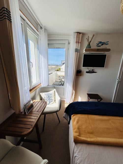 Bright bedroom at La Villa Plein Vent with sea view balcony, TV, armchair, and coastal landscape in Barneville-Carteret