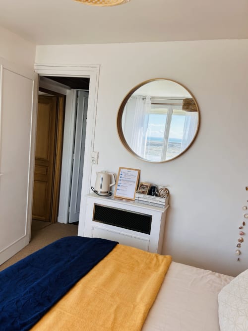 Coastal bedroom at La Villa Plein Vent with circular mirror, sea view, and blue and yellow bedding