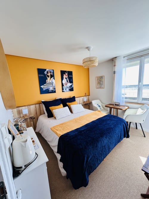 Lumière du Cap bedroom at La Villa Plein Vent B&B with yellow accent wall, navy bedding, and sea view in Barneville-Carteret