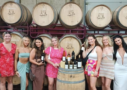 Sete mulheres posando junto a barril de vinho com garrafas em frente à adega da vindima em Albufeira.