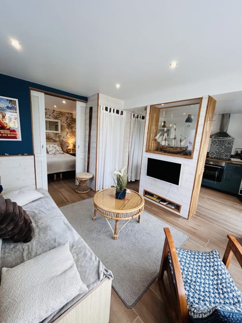 La Bounty cottage living area at La Villa Plein Vent with round wooden table, sofa, TV, bedroom entrance, and kitchen in