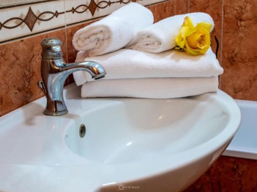 Elegante lavabo della Alla Basilica Rooms con rubinetto cromato, asciugamani arrotolati e rosa gialla a San Giovanni