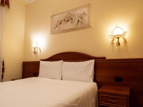 Elegante camera matrimoniale alle Alla Basilica Rooms con pareti giallo caldo, letto in legno e arte classica alle pareti nel rione San Giovanni