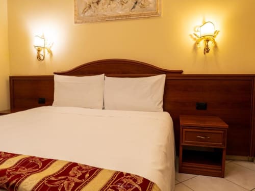 Camera elegante alle Alla Basilica Rooms San Giovanni con letto in legno, biancheria crema e eleganti applique dorate alle pareti