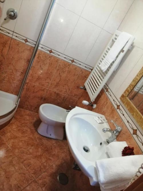 Bagno con piastrelle in terracotta, lavabo bianco, toilette e radiatore presso l'Alla Basilica Rooms a San Giovanni