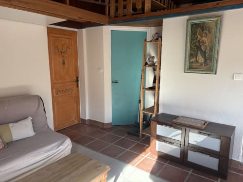 Grand Gîte living room in Calvi with turquoise door, wooden furnishings, terracotta tiles, and framed artwork