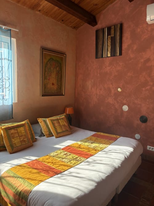 Sunny bedroom at Casa Di Floumy in Calvi with terracotta walls, colorful pillows, and wooden ceiling beams