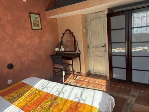 Bright bedroom with terracotta walls, wooden desk, glass doors opening to garden, and colorful bedding at Casa Di Floumy,
