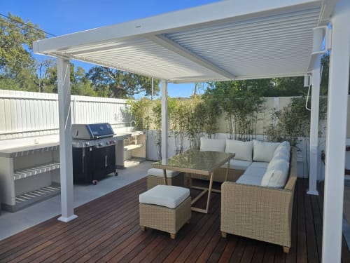 Pérgola branca moderna com área de estar, mesa de jantar e churrascaria no deck de madeira da villa Sesimbra