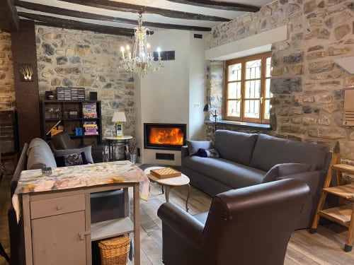 Acogedor salón en Casa Rural Donamariako Benta con muros de piedra, chimenea, asientos de cuero y decoración rústica en Donamaria