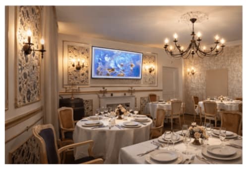 Élégante salle à manger de l'Hôtel de Champagne avec tables rondes, nappes blanches, lustres ornementés et tableaux floraux bleus encadrés