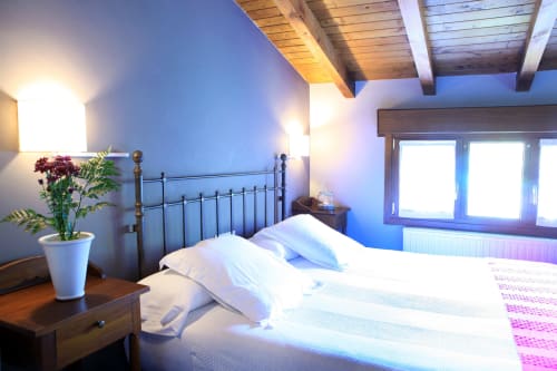 Dormitorio moderno en Casa Rural Donamariako Benta en Donamaria con paredes azules, cama de metal, ropa de cama blanca y vigas de madera