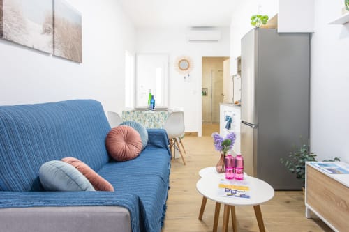 Luminosa sala de estar con sofá azul, mesa blanca y cocina integrada en Casa Libertenio, casa de vacaciones en Los Alcázares