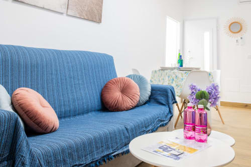 Luminosa sala de estar con sofá de rayas azules, cojines rosas, mesa de centro blanca con flores y acceso a Casa Libertenio