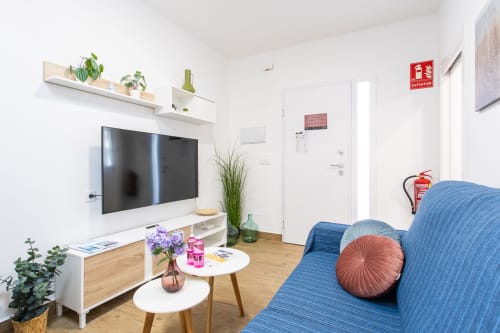 Sala de estar moderna en Casa Libertenio, Los Alcázares, con sofá azul, TV de pared, plantas en maceta y muebles de madera