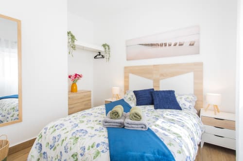 Dormitorio luminoso en Haus Holiday Homes de Los Alcázares con cama de madera, almohadas azules, ropa de cama floral y diseño moderno