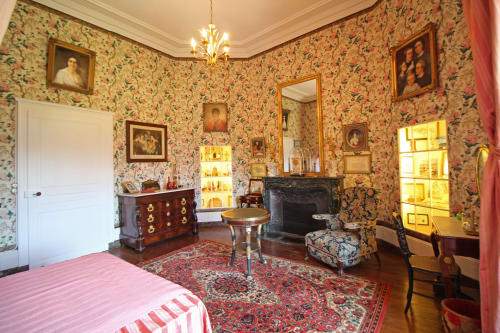 Historic bedroom at Domaine de Bort near Limoges with floral wallpaper, fireplace, period furniture and parquet floors
