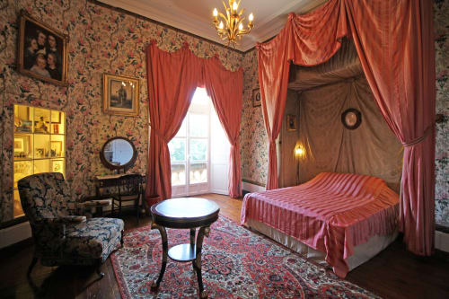 Elegant bedroom at Domaine de Bort with four-poster bed, red drapes, floral wallpaper, and period furnishings