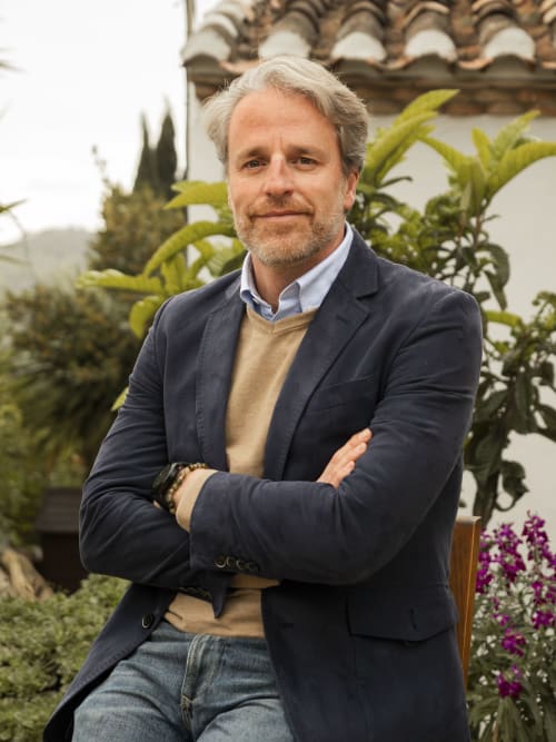 Hombre profesional con blazer azul marino posa en patio mediterráneo con vegetación del hotel Escanda Building Solutions, España