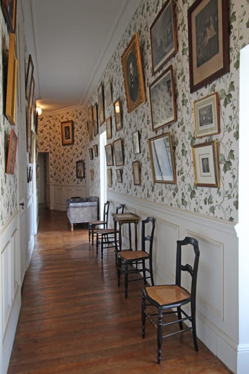 Historic hallway at Domaine de Bort near Limoges with floral wallpaper, framed artwork, wooden chairs, and wooden flooring