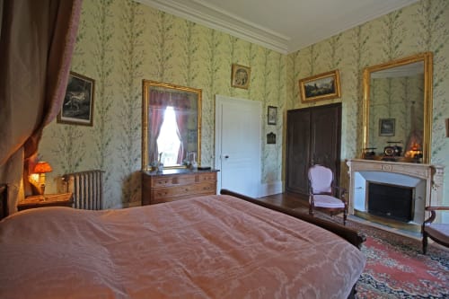Chambre historique élégante au Domaine de Bort avec lit rose, papier peint fleuri, cheminée et mobilier d'époque près de Limoges