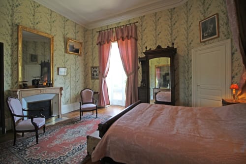 Elegant bedroom at Domaine de Bort with floral wallpaper, fireplace, period furniture, and pink curtains overlooking gardens