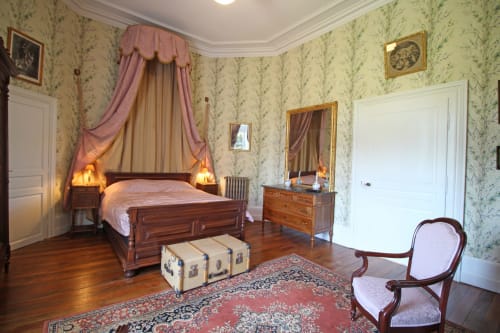 Elegant bedroom at Domaine de Bort with canopied bed, floral wallpaper, wooden furniture, and period decor in La Chambre