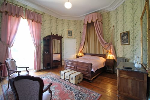 Elegant bedroom at Domaine de Bort B&B with period furnishings, floral wallpaper, pink drapes and wooden bed