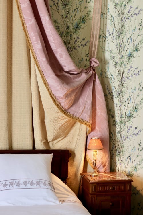 Elegant bedroom at Domaine de Bort near Limoges with layered curtains, bedside lamp, and floral wallpaper