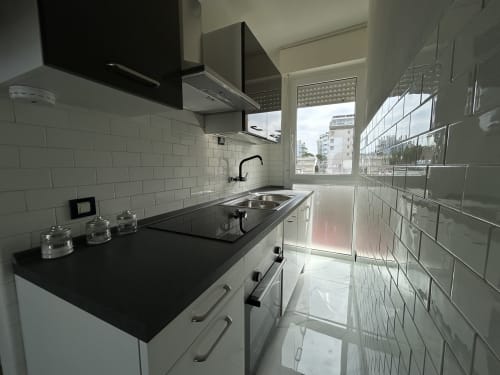 Cucina moderna nell'appartamento Loft Harmonia dell'Anthea Hotel a Lignano Sabbiadoro, con mobili bianchi e piano cucina nero