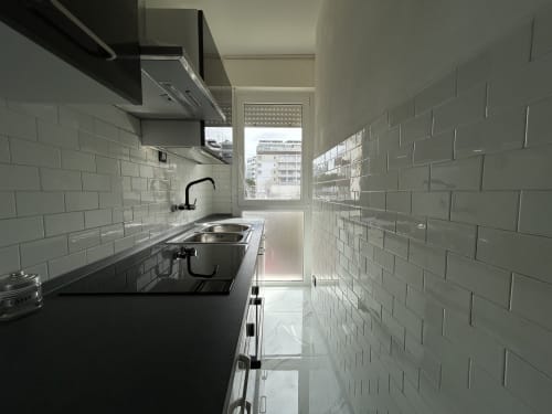 Cucina moderna lineare dell'hotel Anthea a Lignano Sabbiadoro con piastrelle bianche, piano scuro e vista sulla città