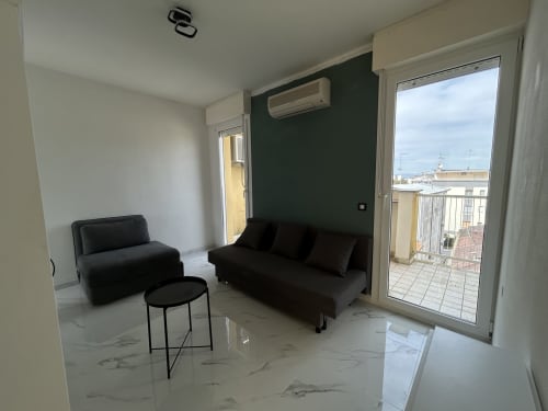 Moderno soggiorno nell'appartamento Loft Harmonia dell'Anthea Hotel, Lignano Sabbiadoro, con divano nero, poltrona, accesso al balcone e