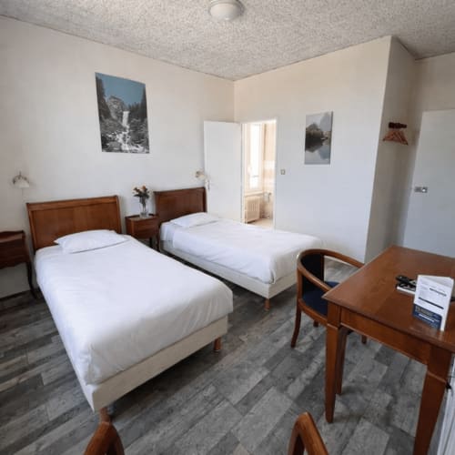 Twin bedroom at Hotel de Champagne in Saint-Dizier with two single beds, wooden furniture, and mountain landscape photographs