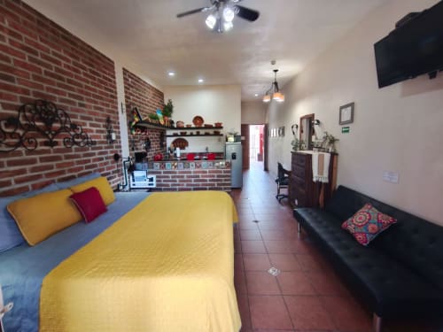 Habitación luminosa de villa con ropa de cama amarilla, pared de ladrillo rojo, cocineta y sofá negro en hotel boutique Punta Perula