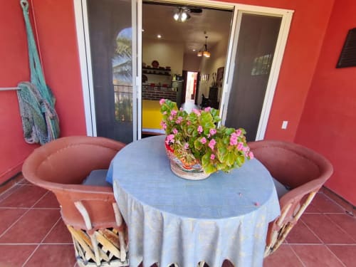 Patio vibrante de Casa Punta Perula con flores rosas en mesa azul, sillas de terracota, muros coralinos y vistas al mar
