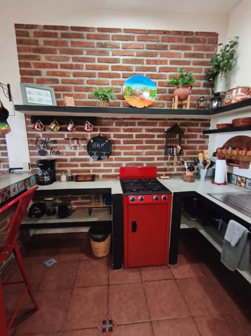 Cocina de villa Casa Punta Perula con estufa roja, salpicadero de ladrillo, estantes abiertos y decoración rústica mexicana en Jal,