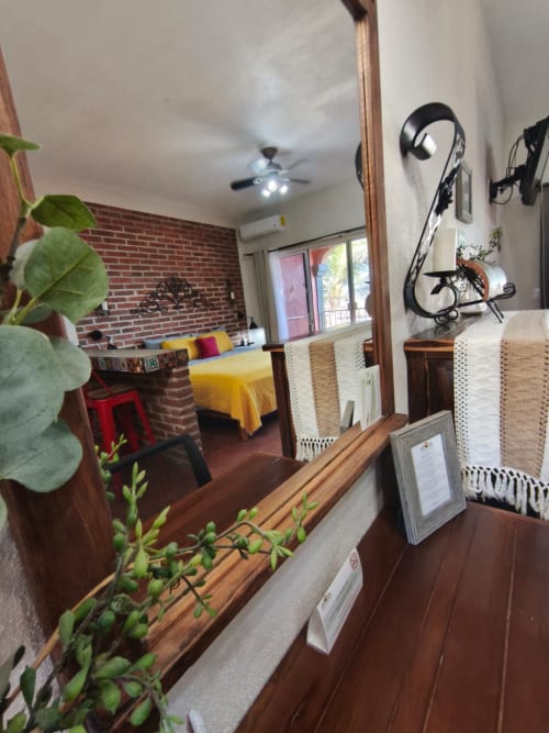 Interior de villa Casa Punta Perula con pared de ladrillo, cama amarilla, muebles de madera, plantas en maceta y almacenamiento de bicicletas